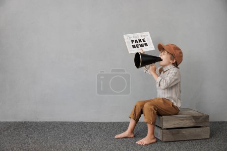 Photo for Newsboy shouting through loudspeaker against grunge wall background. Boy selling fake news. Child wearing vintage costume. Kid holding newspaper. Social media and Internet nerwork concept - Royalty Free Image
