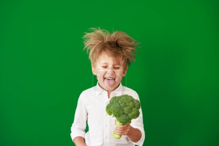 Photo for Surprised child holding broccoli in class. Funny kid against green chalkboard background. Back to school and education concept - Royalty Free Image