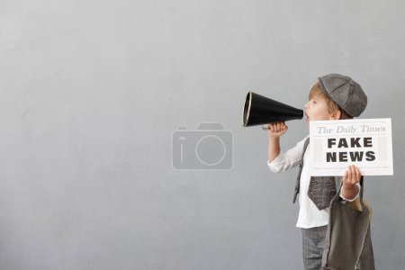 Photo for Newsboy shouting through loudspeaker against grunge wall background. Boy selling fake news. Child wearing vintage costume. Kid holding newspaper. Social media and Internet nerwork concept - Royalty Free Image