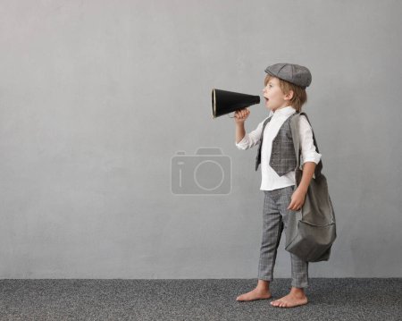 Newsboy schreit durch Lautsprecher gegen Betonwand Hintergrund. Kinderzeitung. Kind im Vintage-Kostüm. Soziales Medien- und Internet-Konzept