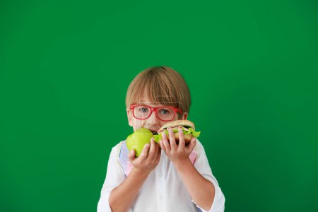 Photo for Funny child student with hamburger and apple in class. Happy kid against green chalkboard. Education and back to school concept - Royalty Free Image