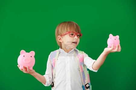Photo for Funny child student holding piggybank in class. Happy kid against green chalkboard. Education and back to school concept - Royalty Free Image