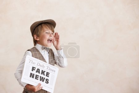 Foto de Newsboy gritando contra el fondo de la pared grunge. Un chico vendiendo noticias falsas. Niño vistiendo traje vintage. Niño sosteniendo el periódico. Concepto de nerwork de redes sociales e Internet - Imagen libre de derechos
