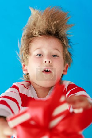 Téléchargez les photos : Surpris enfant tenant cadeau de Noël. Enfant portant un pyjama de Noël rayé sur fond de papier bleu. Concept vacances d'hiver - en image libre de droit