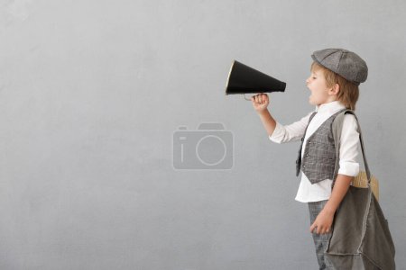 Photo for Newsboy shouting through loudspeaker against grunge wall background. Kid selling newspaper. Child wearing vintage costume. Social media and Internet nerwork concept - Royalty Free Image