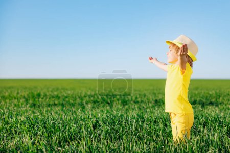 Foto de Feliz niño jugando al aire libre en el campo verde de primavera. Sonriente niño ordenando contra azul verano cielo fondo - Imagen libre de derechos