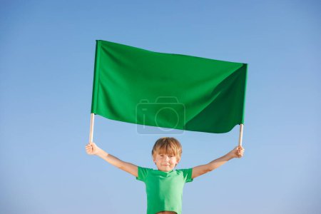 Photo for Happy child holding two wooden sticks with green canvas banner. Kid promotion with textile banner outdoor against blue summer sky background. Ecology and Earth day concept - Royalty Free Image