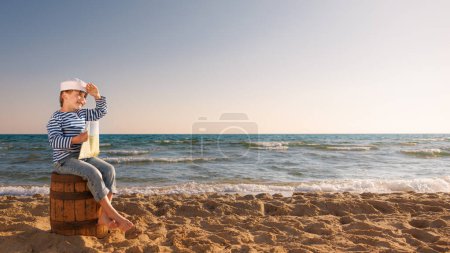 Photo for Child pretend to be sailor. Kid holding map Child sitting on old barrel on the beach. Boy on summer vacation. Adventure and travel concept - Royalty Free Image