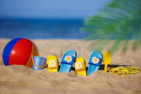 Photo for Kids flip-flops, beach ball and snorkel on yellow sand against blue sea background. Summer vacation concept - Royalty Free Image