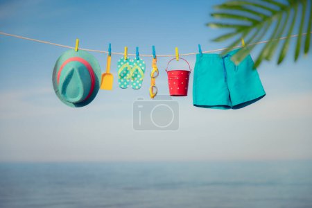 Foto de Sombrero de playa, chanclas y gafas colgando de un tendedero. Cosas para vacaciones contra el cielo azul y el mar. Vacaciones de verano y concepto de viaje - Imagen libre de derechos