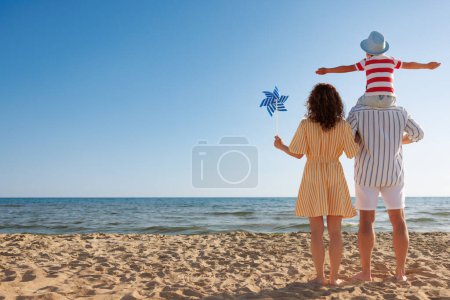 Téléchargez les photos : Bonne famille en vacances d'été. Mère, père et enfant s'amusent sur la plage. Vacances d'été et concept de voyage. Portrait complet ; vue arrière - en image libre de droit