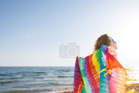 Foto de Mujer feliz en vacaciones de verano. Persona divirtiéndose en la playa. Chica sosteniendo tela de arco iris. Vacaciones de verano y concepto de viaje - Imagen libre de derechos