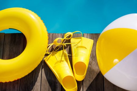 Photo for Fippers and goggles on wooden background. Things for vacation against blue water of swimming pool. Summer holiday and travel concept - Royalty Free Image