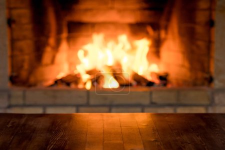 Téléchargez les photos : Vieille table en bois vide contre le feu de bois dans la cheminée. Vacances d'hiver Noël et Nouvel An concept - en image libre de droit