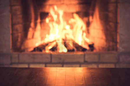 Photo for Empty old wooden table against burning wood in the fireplace. Winter holidays Christmas and New years concept - Royalty Free Image