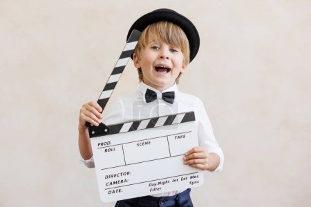 Director shouting against grunge wall background. Boy playing in home. Child wearing vintage costume. Kid holding clapper. Social media and Internet nerwork concept