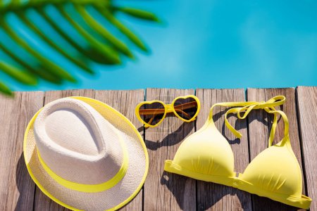 Beach swimsuit and sunglasses on wooden background. Things for vacation against blue water of swimming pool. Summer holiday and travel concept