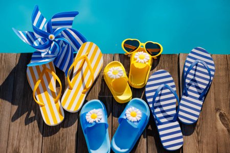 Photo for Beach flip-flops and sunglasses on wooden background. Things for vacation against blue water of swimming pool. Summer holiday and travel concept - Royalty Free Image