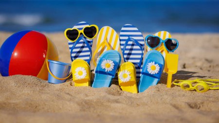 Photo for Family flip-flops, beach ball and snorkel on yellow sand against blue sea background. Summer vacation and travel concept - Royalty Free Image