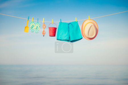 Photo for Beach hat, flip-flops and goggles hanging on a clothesline. Things for vacation against blue sky and sea. Summer holiday and travel concept - Royalty Free Image