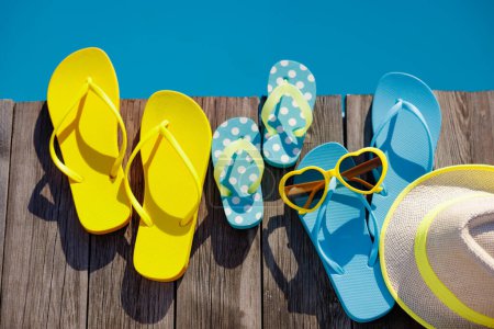 Téléchargez les photos : Tongs de plage et lunettes de soleil sur fond bois. Choses pour les vacances contre l'eau bleue de la piscine. Vacances d'été et concept de voyage - en image libre de droit