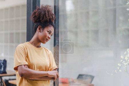 Mujer afroamericana con el pelo afro de pie, mirando hacia la ventana. La mujer frustrada y confundida parece infeliz, lidiando con problemas de vida personal