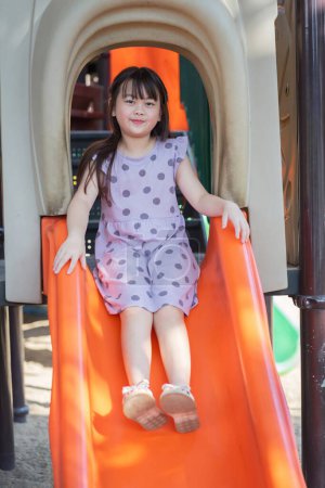 happy preschool girl playing on a slide in the playground in a summer park.