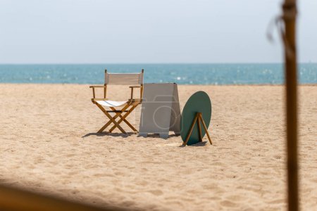 Photo for Directors chair and blank outdoor stand mockup poster display on the beach - Royalty Free Image