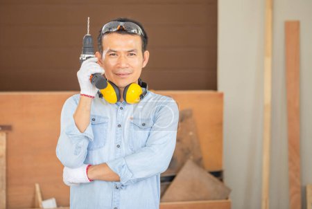 Photo for Cheerful carpenter holding electric screwdriver in the workshop, Technical man doing woodwork in carpentry - Royalty Free Image