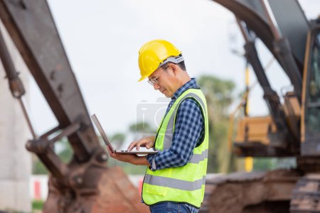 Téléchargez les photos : Un ingénieur vérifie le projet sur le chantier, un homme en casque avec un ordinateur portable sur le chantier de construction de l'infrastructure - en image libre de droit