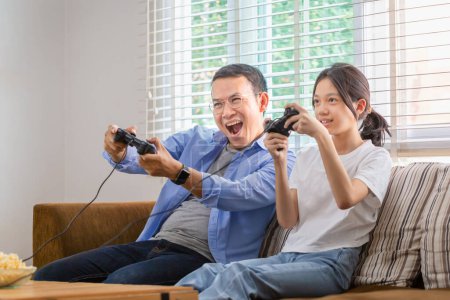 Téléchargez les photos : Asiatique père et fille jouer à des jeux vidéo à la maison, Les gens faisant des activités et des concepts de famille - en image libre de droit