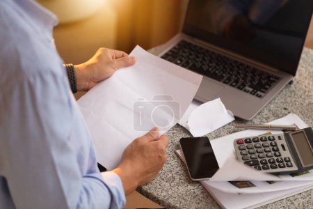 Photo for Asian man working with documents and laptop, man checking their bills - Royalty Free Image
