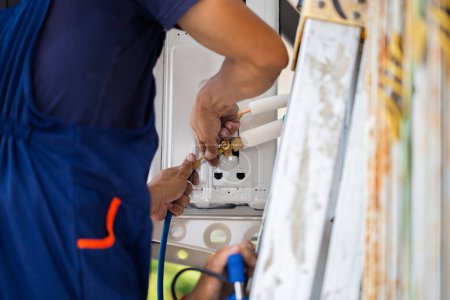 Foto de Joven reparador que fija la unidad del acondicionador de aire, hombre técnico asiático que instala un aire acondicionado en una casa del cliente, conceptos de mantenimiento y reparación - Imagen libre de derechos