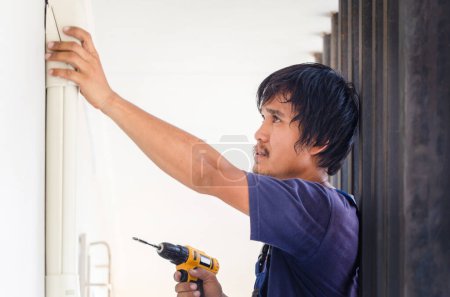 Téléchargez les photos : Asiatique technicien homme installant la climatisation dans une maison cliente, Jeune réparateur réparateur unité de climatisation, Entretien et réparation concepts - en image libre de droit