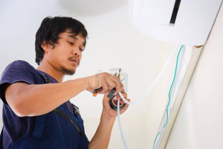 Téléchargez les photos : Technicien installant la climatisation dans une maison cliente, électricien montant les fils dans l'unité de climatisation, réparateur fixant l'unité de climatiseur, concepts d'entretien et de réparation - en image libre de droit