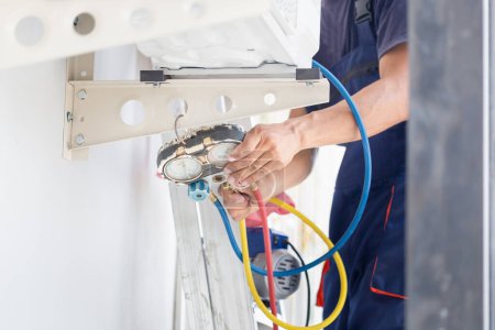 Foto de Reparador que fija la unidad del acondicionador de aire, técnico asiático que instala un aire acondicionado en una casa del cliente, conceptos del mantenimiento y de la reparación - Imagen libre de derechos