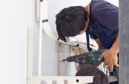 Téléchargez les photos : Technicien homme avec perceuse à marteaux installant un climatiseur dans une maison cliente, Jeune réparateur réparateur unité de climatisation, concepts d'entretien et de réparation - en image libre de droit