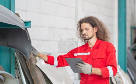 Foto de Hombre mecánico con tableta digital que inspecciona el stock de piezas de automóviles en el almacén del garaje, joven mecánico que trabaja en el taller de reparación de automóviles - Imagen libre de derechos