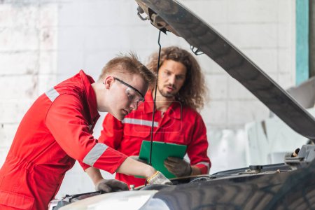 Photo for Technician team checking modern car at garage, Young Caucasian car mechanic with a checklist, Mechanics in uniform are working in auto service, Car repair and maintenance - Royalty Free Image