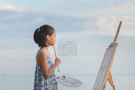 Foto de Retrato de una niña pintando en el lienzo de la playa. Feliz niña haciendo un dibujo al aire libre - Imagen libre de derechos
