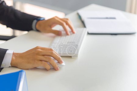 Foto de Primer plano de la mano masculina haciendo clic ratón digital inalámbrico que trabaja con el ordenador de escritorio en el escritorio de la oficina - Imagen libre de derechos