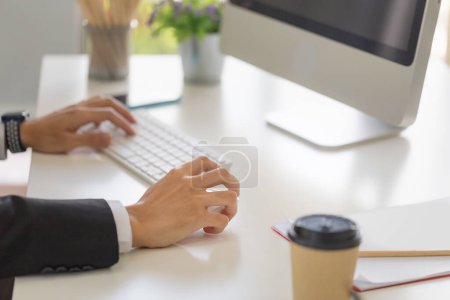 Foto de Primer plano de la mano masculina haciendo clic ratón digital inalámbrico que trabaja con la computadora de escritorio en el escritorio de la oficina - Imagen libre de derechos