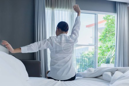 Photo for Back view of woman wake up in the morning and stretching hand on the bed - Royalty Free Image