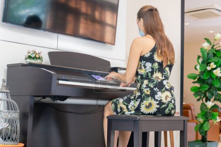 Photo for Woman in dress playing piano in living room, Young girl playing grand piano at home - Royalty Free Image