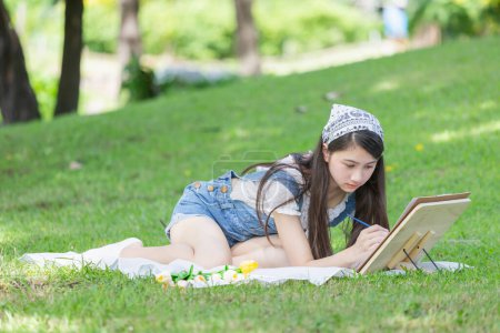 Foto de Adolescente asiática dibujando un cuadro en el parque con caballete, paleta y pincel - Imagen libre de derechos