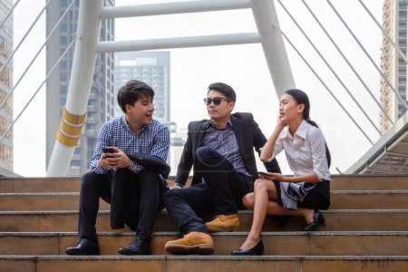 Téléchargez les photos : Jeune équipe d'affaires asiatiques discutant le matin, Jeunes gens d'affaires assis dans les escaliers avec des amis, Les gens d'affaires se rencontrent et partagent des idées - en image libre de droit