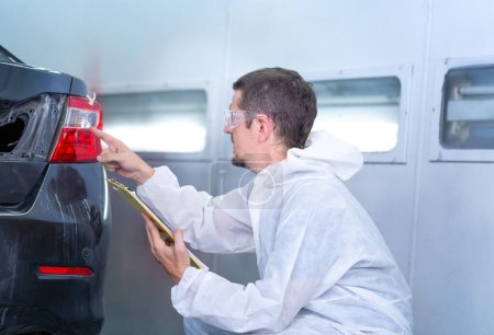 Photo for Worker man holding clipboard checklist of the car at the garage, Mechanic painting car in the chamber. Garage painting car service repair and maintenance - Royalty Free Image