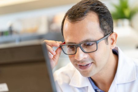 Photo for Cheerful optometrist man holding eyeglasses in optics store, Indian man choosing glasses at optics shop - Royalty Free Image