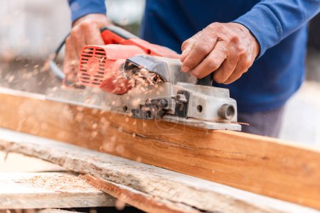 Foto de Carpintero con cepilladora eléctrica para alisar la madera, máquina de carpintería, tableros de cepillado hombre con herramientas eléctricas - Imagen libre de derechos