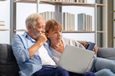 Photo for Senior couple spending time together in the living room, woman and man using laptop and digital tablet on the cozy sofa at home - Royalty Free Image